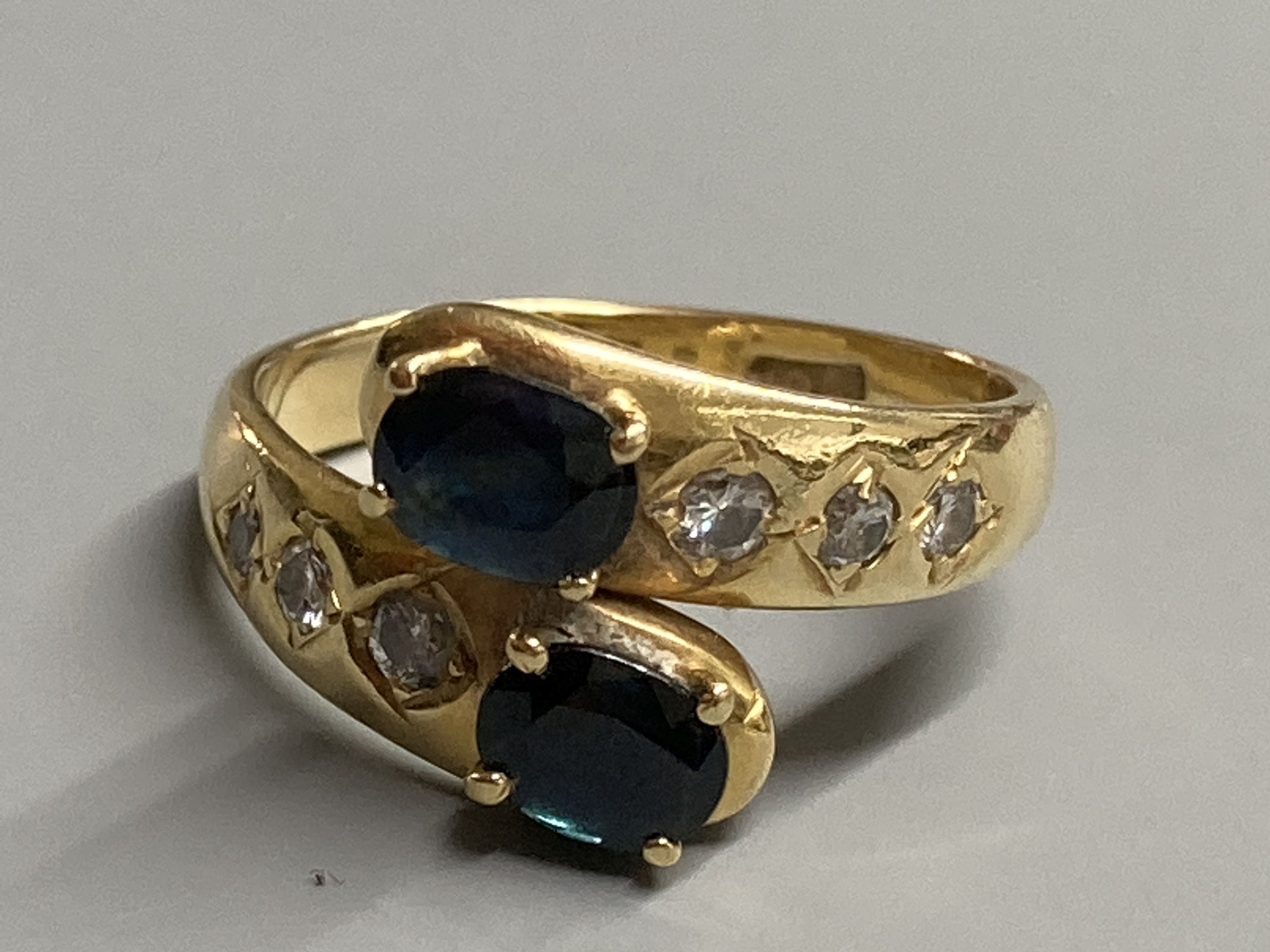 A modern 18ct and two stone sapphire crossover ring, with diamond set shoulders, size P, gross 5.4 grams.